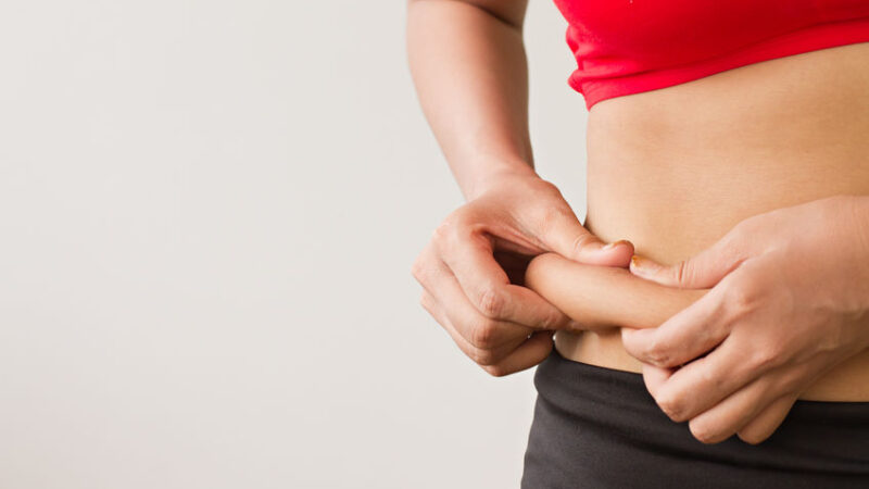 32498579 - woman's hand holding excessive belly fat